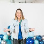 Photo of Emilie Steinmann, a woman wearing a jean jacket throwing confetti and standing in front of blue balloons