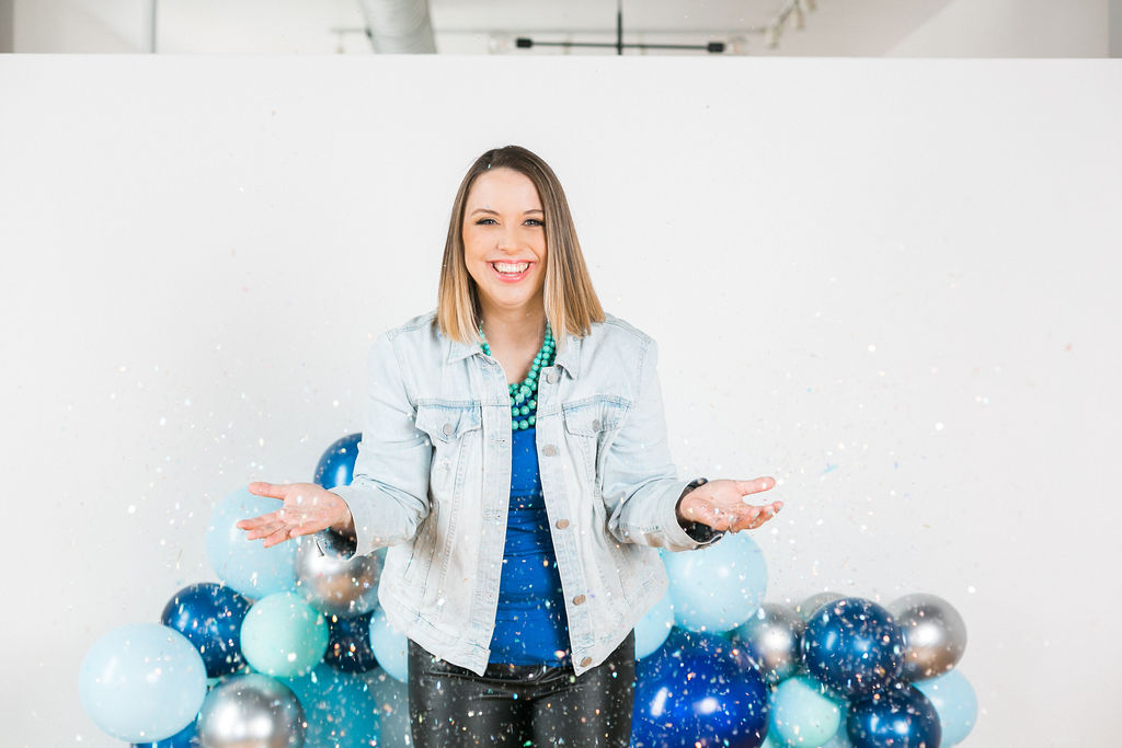 Photo of Emilie Steinmann, a woman wearing a jean jacket throwing confetti and standing in front of blue balloons